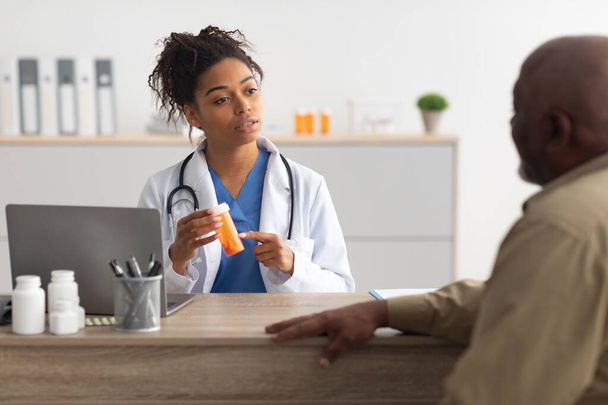 Vrouwelijke zwarte arts tonen pillen aan mannelijke patiënt - Foto, afbeelding