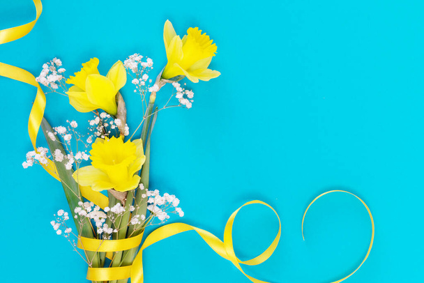 Bouquet of yellow daffodils with gold ribbon on blue background - Valokuva, kuva