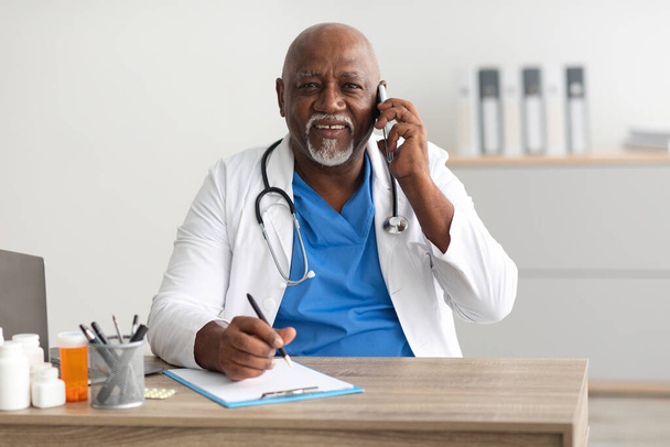 Portret uśmiechniętego lekarza patrzącego na aparat mówiącego przez telefon - Zdjęcie, obraz