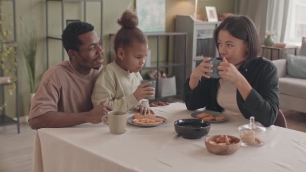 médio lentidão de feliz interracial família de três sentado no cozinha mesa juntos beber chá e falando - Filmagem, Vídeo