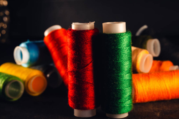 multi-colored spools of thread on a black background - Фото, изображение