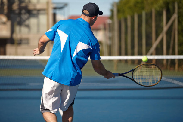 Returning it with force. Rear view of a young man about to hit a tennis ball. - 写真・画像