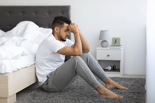 Life Troubles. Depressed Pensive Young Arab Man Sitting On Floor Near Bed - Photo, Image