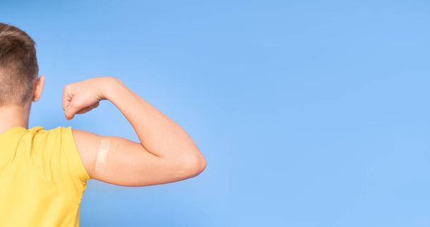 Un adolescente con un parche en el brazo cierra el puño y dobla el bíceps después de la vacunación. Vacuna inyectable contra covid, cuidado de la salud para niños. lugar para el texto. - Foto, imagen