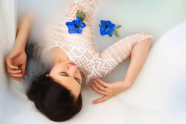 Spa schoonheid model meisje nemen melkbad, spa en huidverzorging concept. Schoonheid jonge vrouw met heldere make-up en blauwe roos bloem ontspannen in melkbad. Verjonging. - Foto, afbeelding