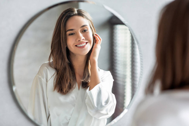 Koncepcja piękna. Portret atrakcyjnej szczęśliwej kobiety patrzącej na lustro w łazience - Zdjęcie, obraz
