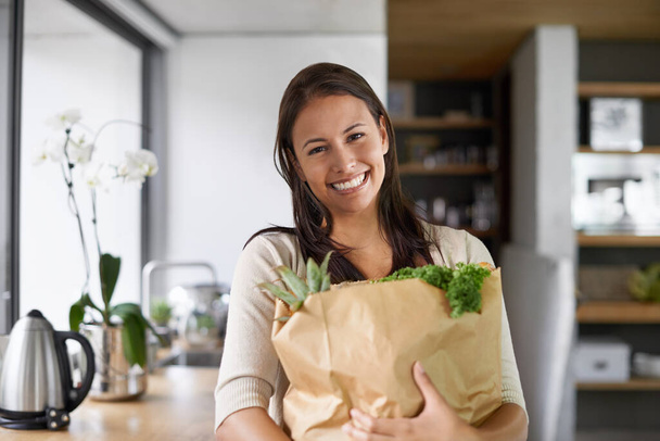 I only buy organic. A young woman standing in her kitchen holding a bag of groceries - portrait. - Foto, Imagem