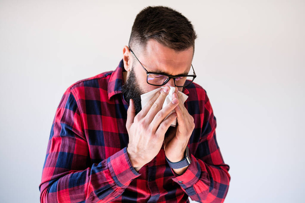 Portret van een man die zijn neus snuit vanwege allergie. Kopieer ruimte op de afbeelding voor uw tekst of advertentie. - Foto, afbeelding