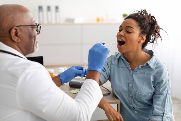 Doktor potansiyel olarak enfekte olmuş siyah kadından PCR testi örneği alıyor. - Fotoğraf, Görsel