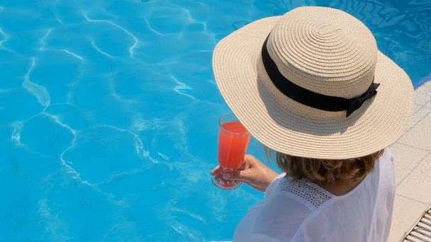Kobieta w słomkowym kapeluszu relaksuje się w pobliżu basenu, pije różowy koktajl, zamyka się. Koncepcja nastroju letniego - Zdjęcie, obraz