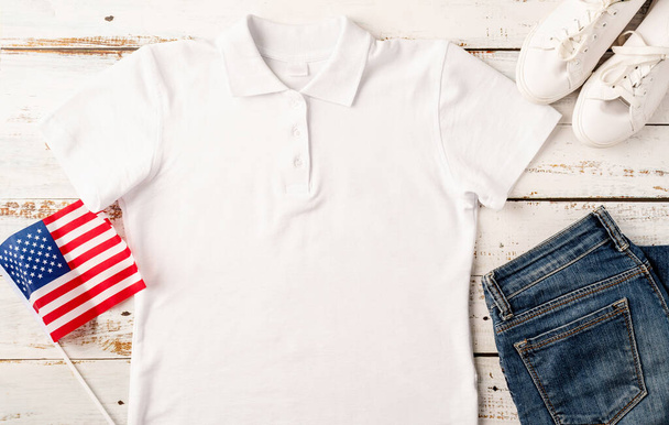 USA Memorial day, Presidents day, Veterans day, Labor day, or 4th of July celebration. Mockup design white polo t shirt for logo, top view on white wooden background with US flag, shoes and jeans - Zdjęcie, obraz