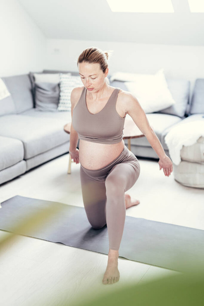 Jovem bela mulher grávida treinando pilates em casa em sua sala de estar. Estilo de vida saudável e gravidez ativa e conceito de maternidade. - Foto, Imagem