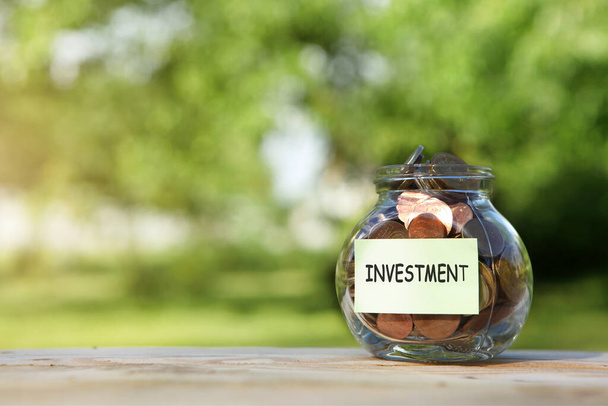  Investment. Glass jar with coins, on a wooden table, on a natural background.  - Photo, Image