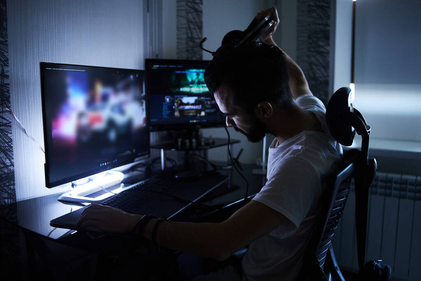 a young 30-year-old gamer is sitting at a computer, playing computer games, nervous, angry, worried.selective focus with low depth of focus. - 写真・画像