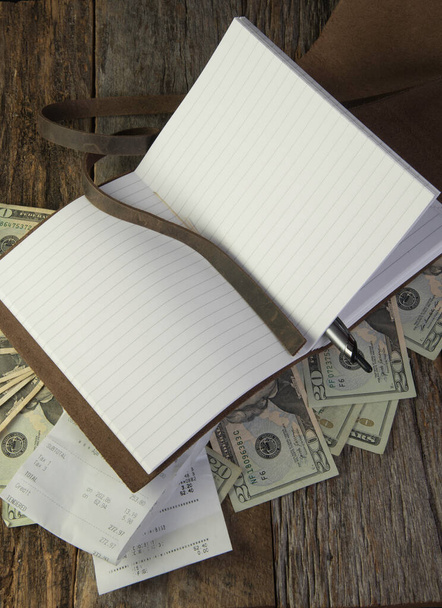 Pusty papier podszyty w skórzanym dzienniku z pieniędzmi i kwitami spożywczymi na drewnianym tle.  - Zdjęcie, obraz