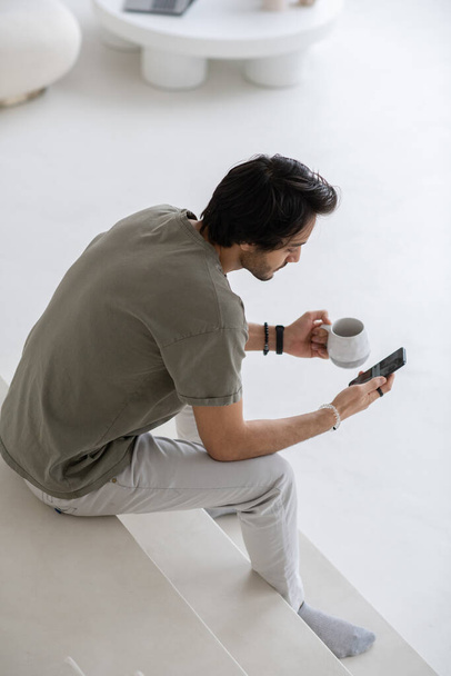 Fiatal modern menedzser mobiltelefonnal ül a fehér lépcsőn, és SMS-t - Fotó, kép