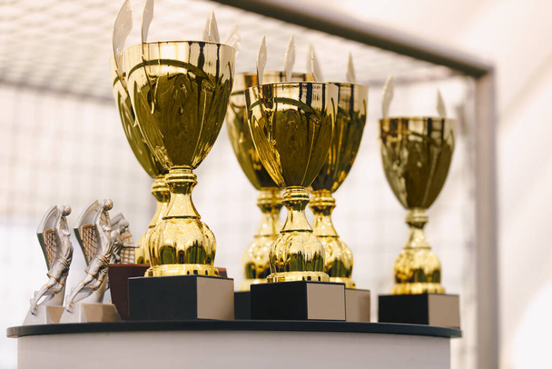 Kuva pöydällä seisovien kultaisten palkintojen joukosta. Kultaiset kupit urheilukilpailun voittajille - Valokuva, kuva
