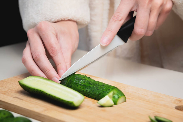 Close-up of female hands cutting fresh cucumbers on a wooden cutting board - 写真・画像