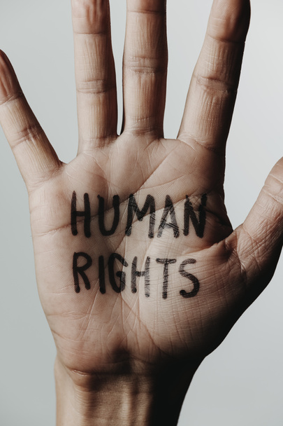 close-up van de hand van een man met de tekst mensenrechten geschreven in zijn handpalm, op een gebroken witte achtergrond - Foto, afbeelding