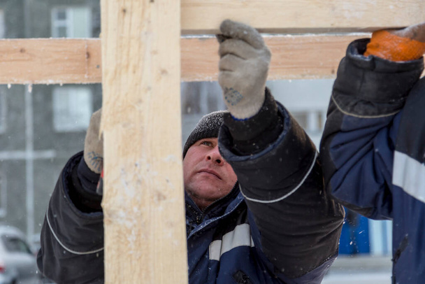 Ein Bauarbeiter in blauer Jacke mit einem Hammer in der Hand hämmert einen Nagel - Foto, Bild