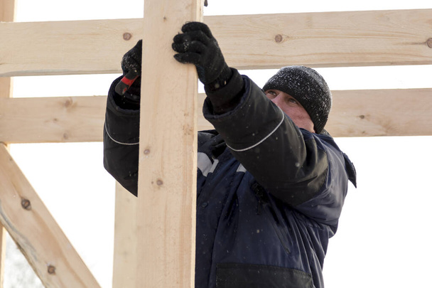 Будівельник в синій куртці з капюшоном з дошкою в руці на установці дерев'яної гірки
 - Фото, зображення