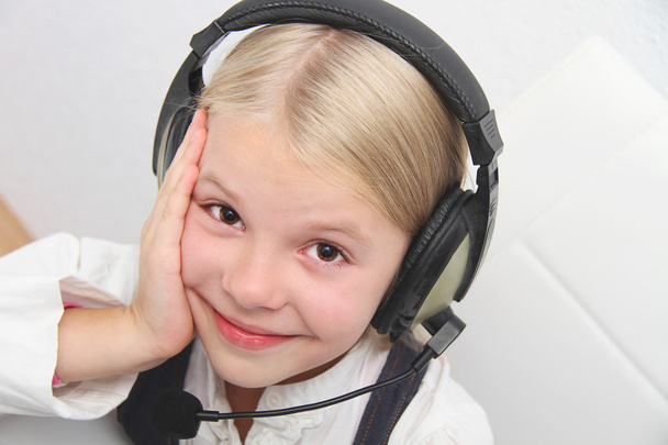 Llittle girl senta-se na frente de um laptop com fones de ouvido e aprender
 - Foto, Imagem