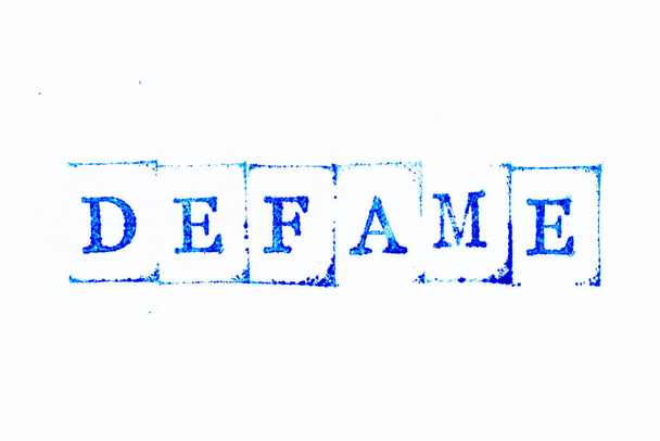 Sello de goma de tinta de color azul en difamación de palabra sobre fondo de papel blanco - Foto, Imagen
