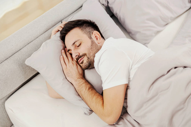 Ένας νυσταγμένος άντρας κοιμάται σφιχτά στο άνετο κρεβάτι του.. - Φωτογραφία, εικόνα