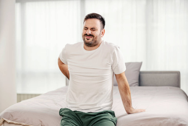 A morning man having back pain in the bedroom. - Фото, зображення