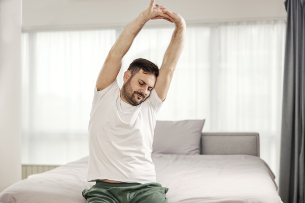 A morning man stretching and waking up in his cozy bedroom. - Foto, Bild
