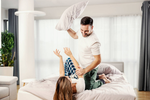 Um casal de manhã brincalhão tendo travesseiro luta na cama em seu apartamento. - Foto, Imagem