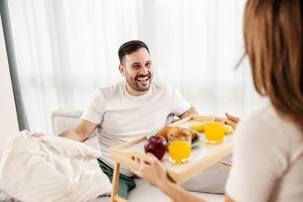 Счастливый человек завтракает в постели, которую принесла его жена в их уютном доме.. - Фото, изображение