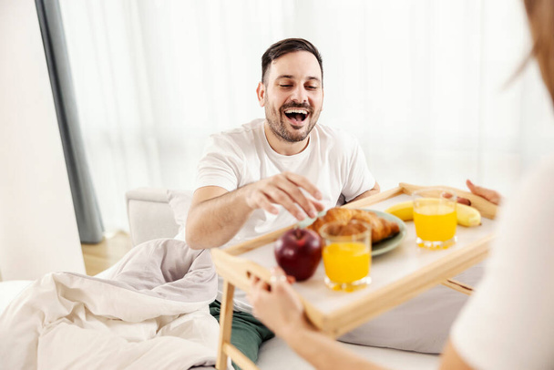 Un uomo felice che fa colazione nel letto portato da sua moglie nella loro accogliente casa. - Foto, immagini