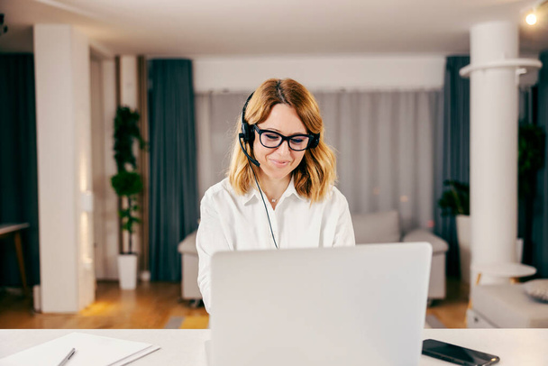 Une femme d'affaires heureuse ayant un appel vidéo sur l'ordinateur portable et travaillant en ligne depuis sa maison confortable. - Photo, image