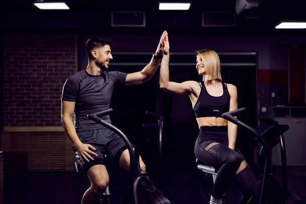 Sporty couple on exercise bikes in a gym accomplished a goal. Teamwork concept. - Фото, изображение