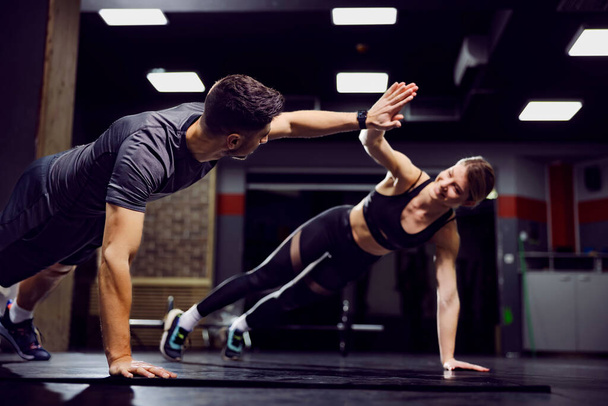 Fitness couple practicing together and clapping with hands in plank position in a gym. - Фото, изображение