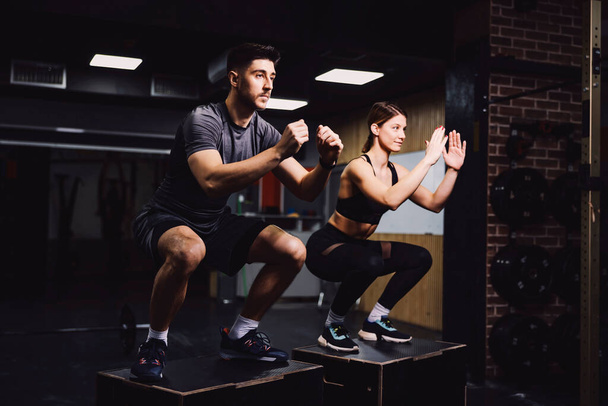 A dedicated sporty couple doing squats in a gym and practicing functional exercises. - Foto, Imagen