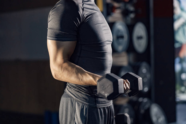Homme musculaire inconnu faisant des exercices pour les biceps avec haltère dans une salle de gym. - Photo, image