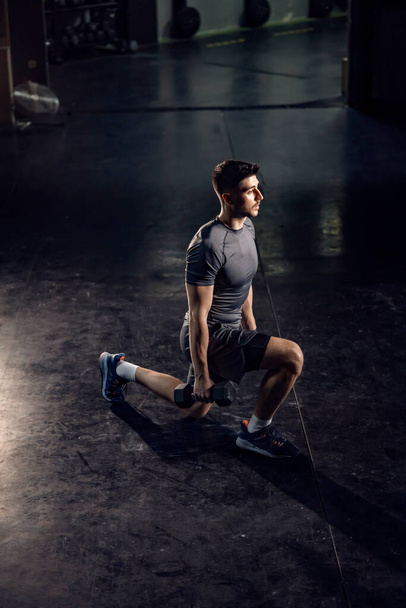 A sporty man doing lunges with dumbbells in a gym, - 写真・画像