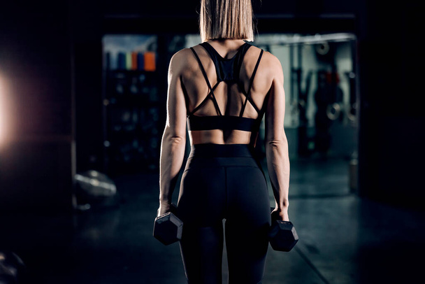 Вид ззаду сильної жінки, що практикує в спортзалі з гантелями
. - Фото, зображення