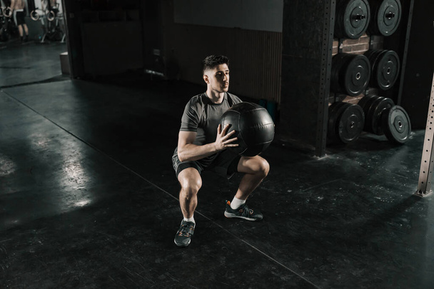 Ένας δυνατός άντρας κάνει λειτουργικές ασκήσεις με ιατρική μπάλα στο γυμναστήριο.. - Φωτογραφία, εικόνα