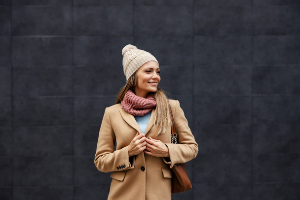 Ženský módní a ženský styl. Stylová šťastná mladá žena v kabátě, šále a šátku, stojící venku a rozepínající knoflík. - Fotografie, Obrázek