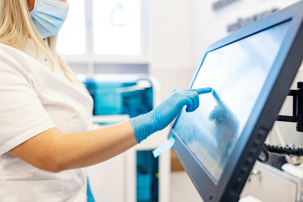 Modernia teknologiaa laboratoriossa. Sairaanhoitaja seisoo koneen vieressä analysoimassa verinäytteitä ja ohjelmoimassa niitä. Hoitaja koskettaa kosketusnäyttö ja ohjelmointi kone. - Valokuva, kuva