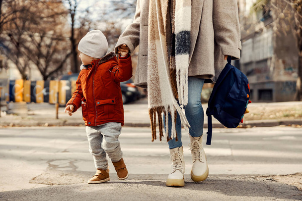 Eine Mutter bringt ihren kleinen Sohn in den Kindergarten und überquert eine Straße. - Foto, Bild