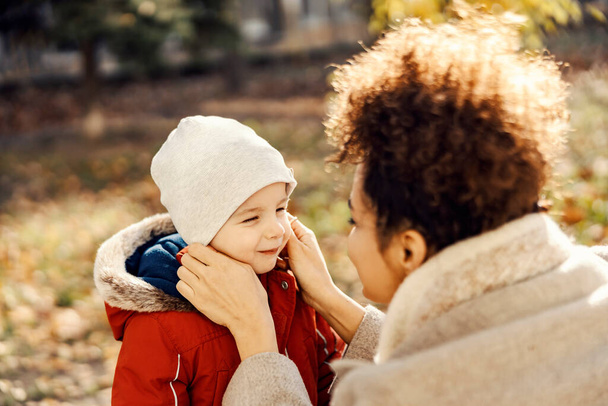 Ein zartes Kindermädchen passt einem kleinen Jungen bei kaltem Wetter eine Mütze an, damit er sich nicht erkältet. - Foto, Bild