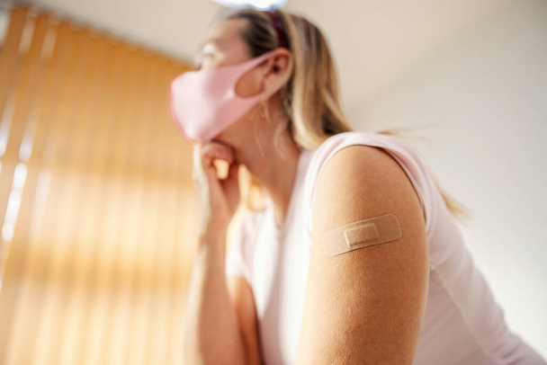 Sluiten van de schouder van een vrouw met lijmpleister na covid 19 vaccin. Immunisatie, inenting, vaccinatie en medische zorg. - Foto, afbeelding