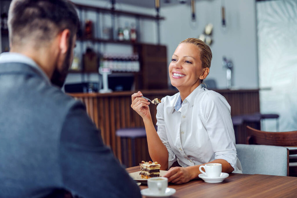 Uma mulher loira feliz está sentada no restaurante com seu cônjuge e comendo bolo de nougat para a sobremesa. Casal comer bolo no restaurante. - Foto, Imagem