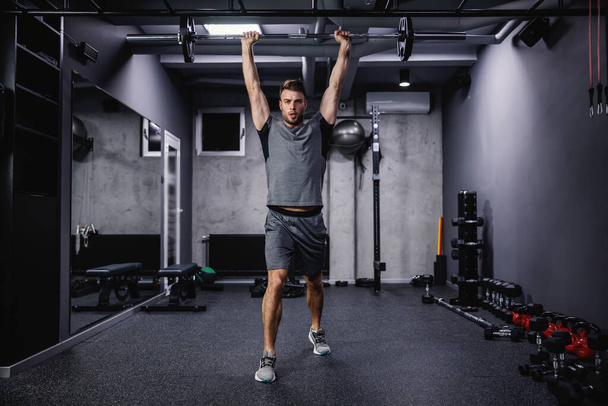Ein muskulöser Sportler stemmt Gewichte in einer Turnhalle. - Foto, Bild