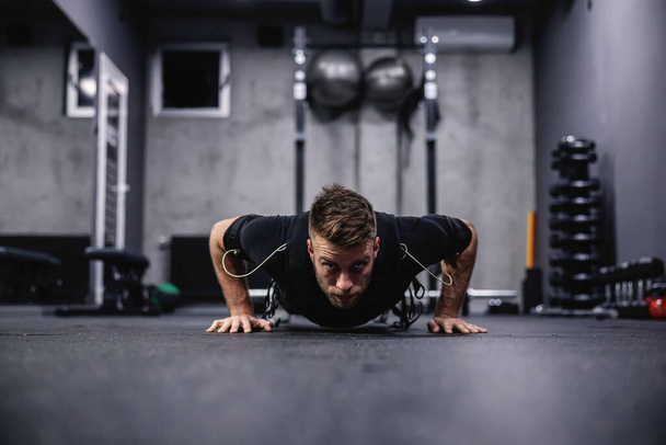 A male fitness coach in a special suit for EMS technology performing arm and chest exercise and push ups in a modern gym concept. Revolution in training, body rehabilitation - Fotografie, Obrázek