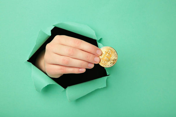 Female hand with coin of bitcoin punching through the paper. Top view - Fotografie, Obrázek